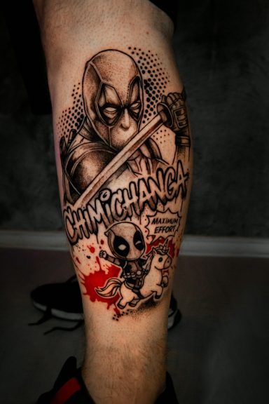 Tattoo eines Superhelden mit Schwert, umgeben von bunten Elementen und Text.