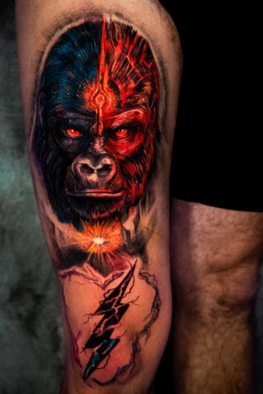 Bunter Tattoo eines Gorilla-Gesichts mit elektrischen Blitzen auf dem Oberschenkel.