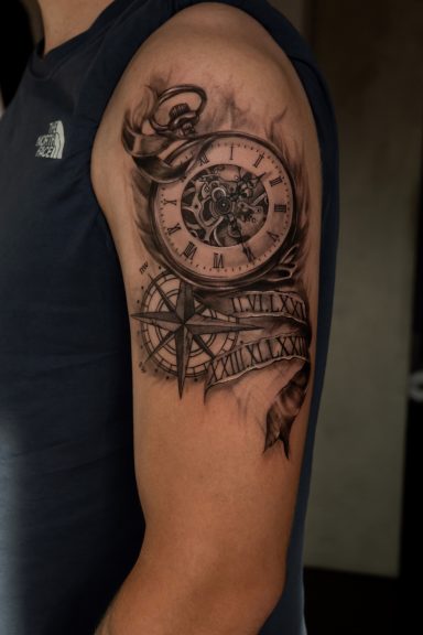 Tattoo eines Uhrwerks mit einem Kompass, künstlerisch auf dem Oberarm dargestellt.