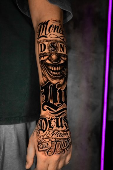 Tattoo auf dem Unterarm mit einem lachenden Gesicht und Schriftzügen.