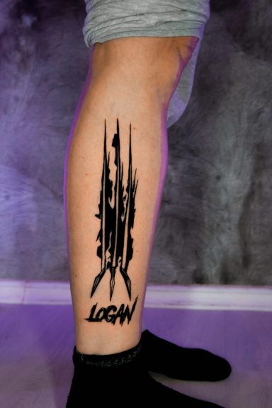 Tattoo auf dem Unterschenkel mit dem Schriftzug "WOLVERINE" und klauenähnlichen Motiven.